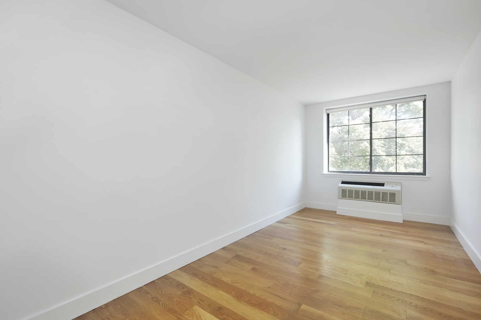 Bedroom at 83 Bushwick Place apartments in Brooklyn with an a/c unit, hardwood floors, and a large window.