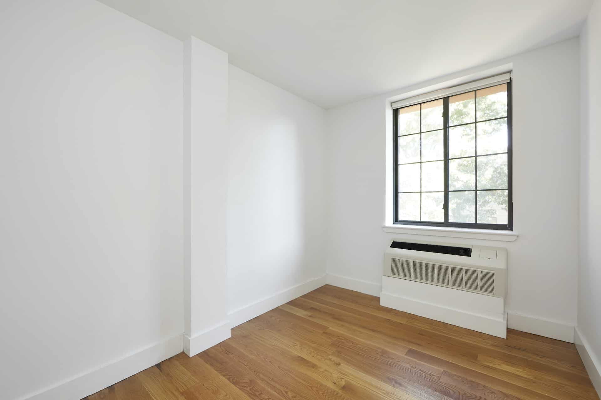Bedroom at 83 Bushwick Place apartments in Brooklyn with hardwood floors, a/c unit and a large window.