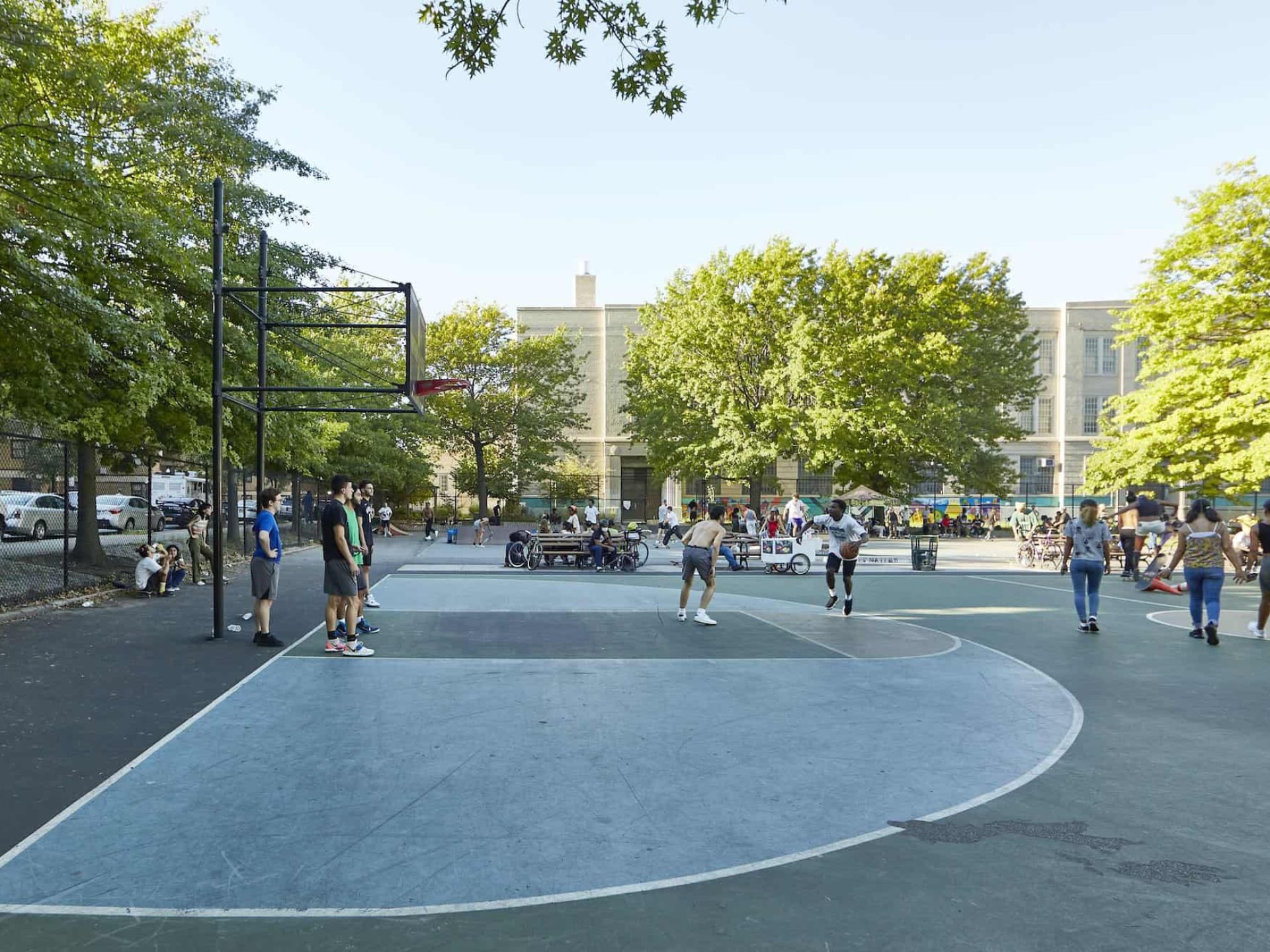 Basketball courts in the Williamsburg neighborhood with people playing basketball and courts bordered with a fence and trees.
