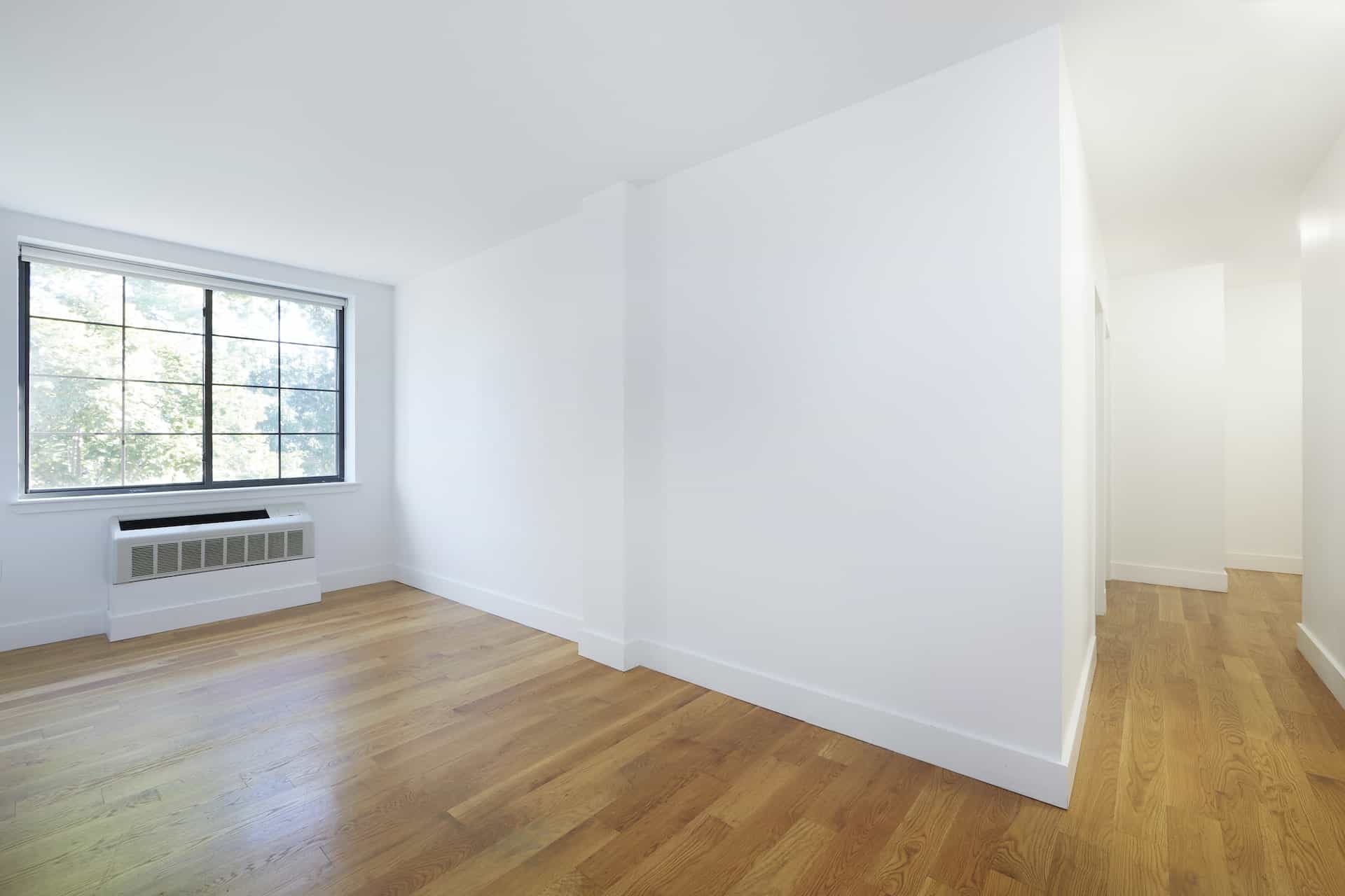 Living room at 83 Bushwick Place apartments in Brooklyn with large windows, hardwood floors, mounted a/c unit and hallway.