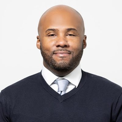 Head shot of Abode Residential licensed real estate agent Abraham Caro. Man with shaved head, white shirt and blue sweater.