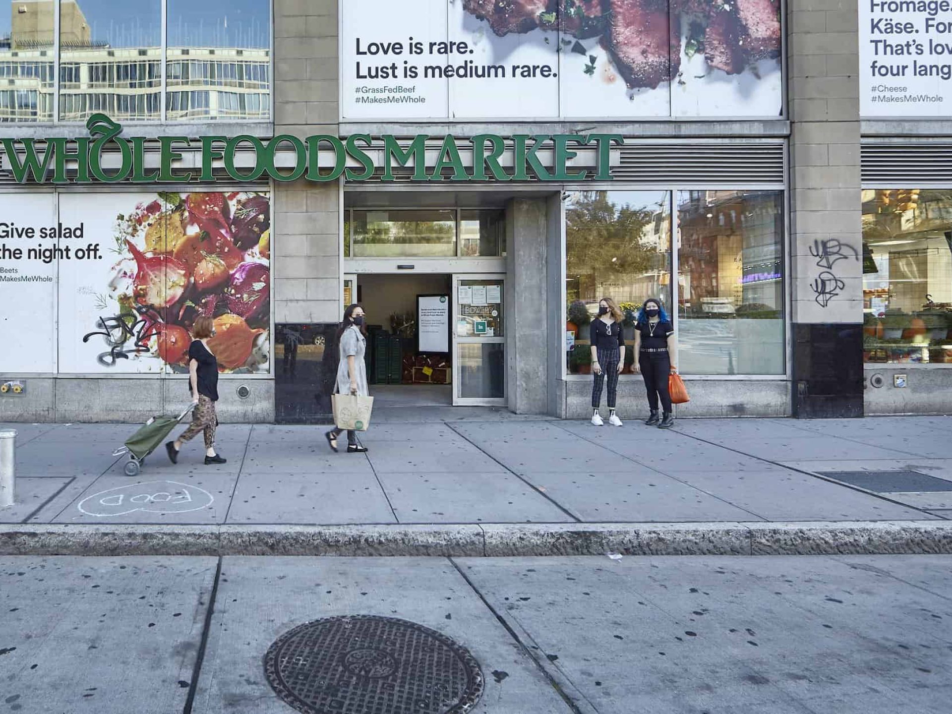 Street view of entrance to Whole Foods Market in Noho. Open sliding door with people standing and walking outside.