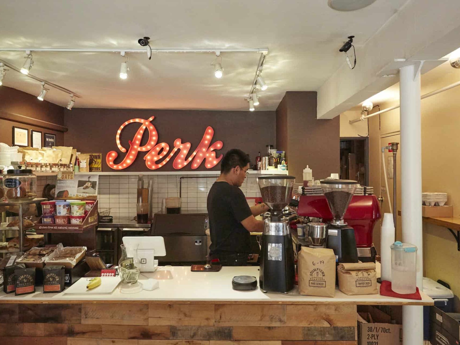 Interior of "Perk" coffee shop in Murray Hill. Lighted business sign on the back wall and a counter with coffee on display.