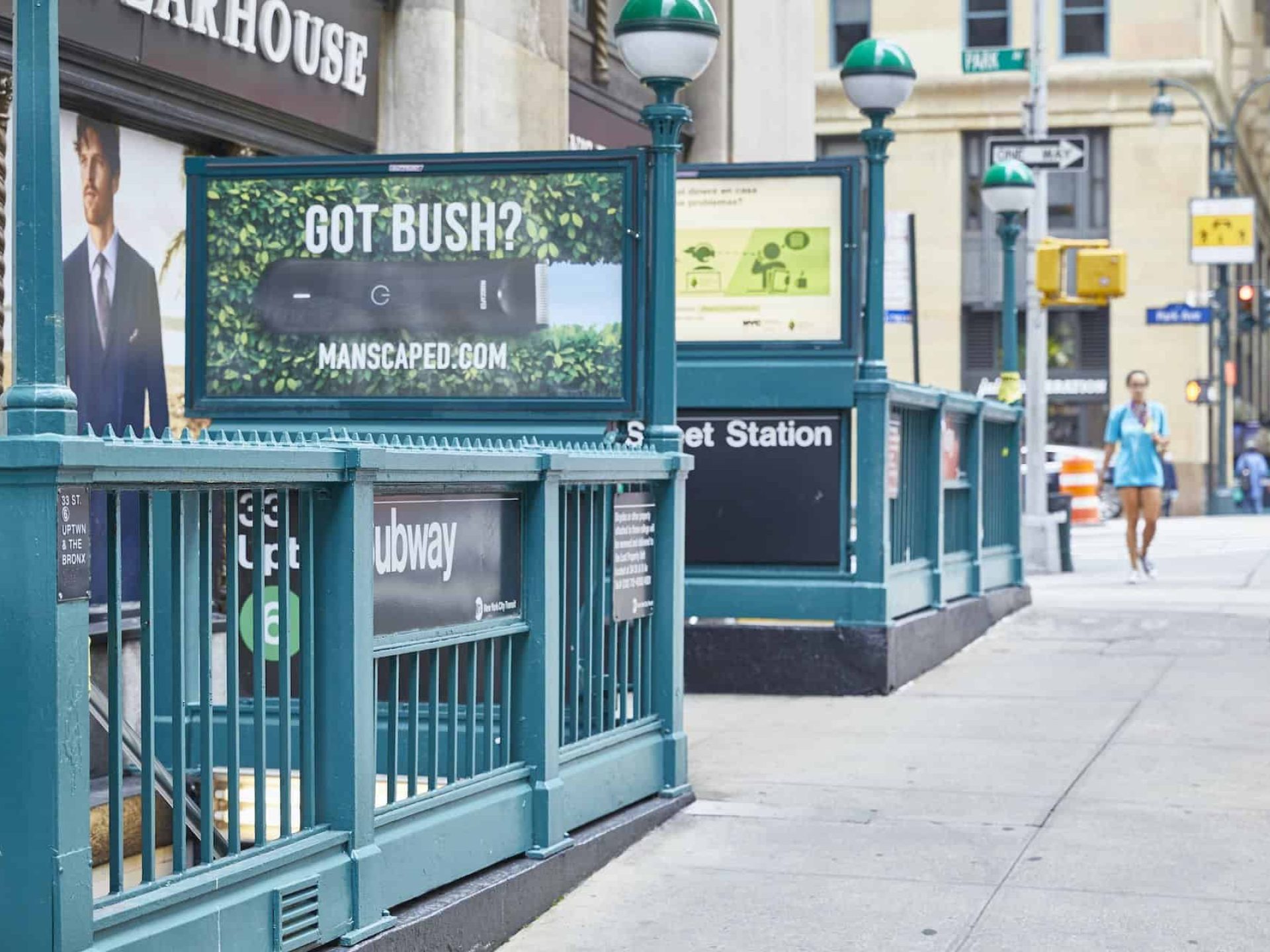 Sidewalk view of the 33rd Street subway entrance in New York. Green railings with subway sign and advertising billboards.